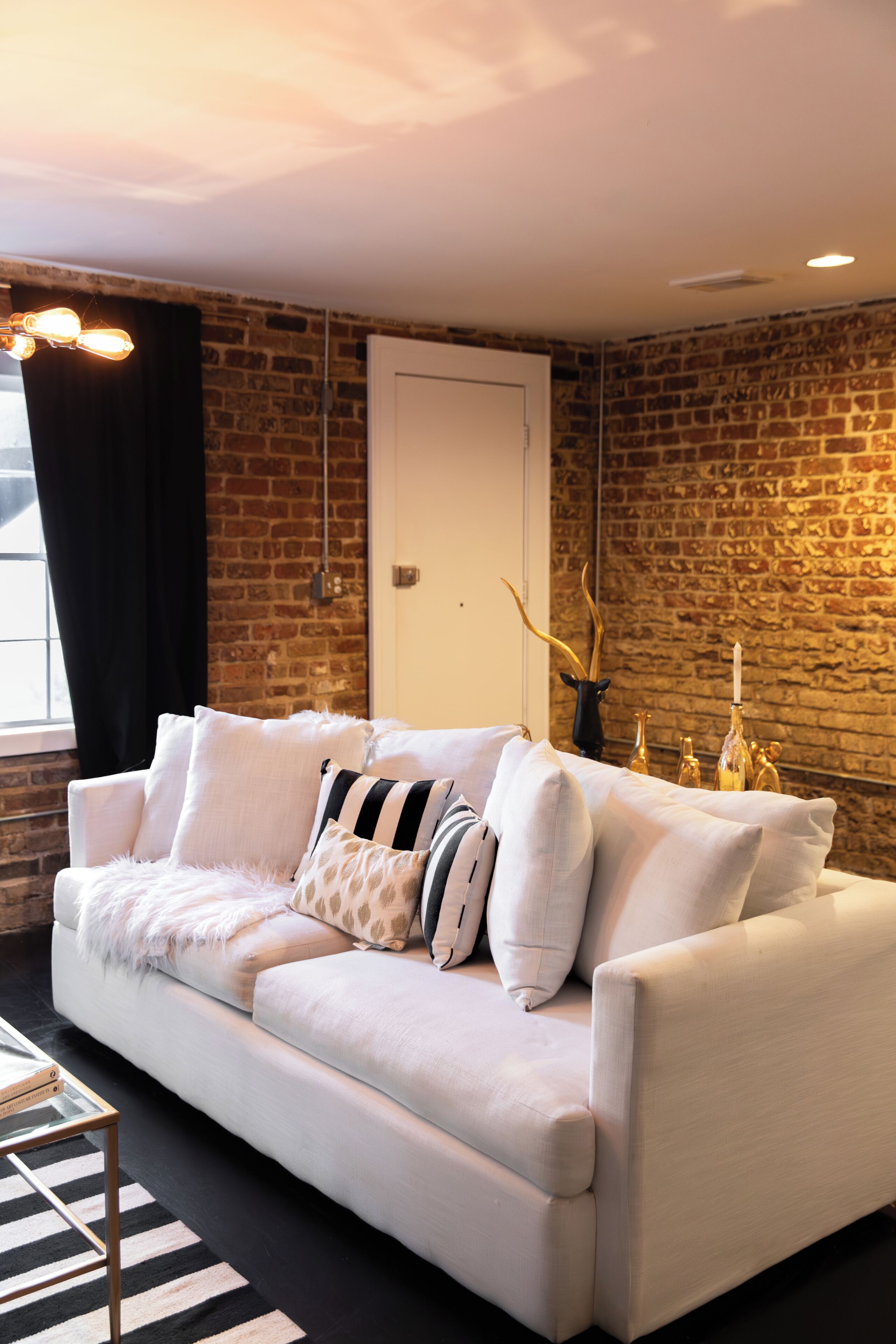 A white sofa with patterned cushions, a glass coffee table, and a black and white striped pillow.