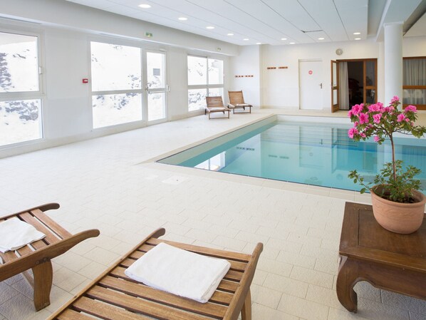 An indoor swimming pool with wooden lounge chairs and a potted plant.