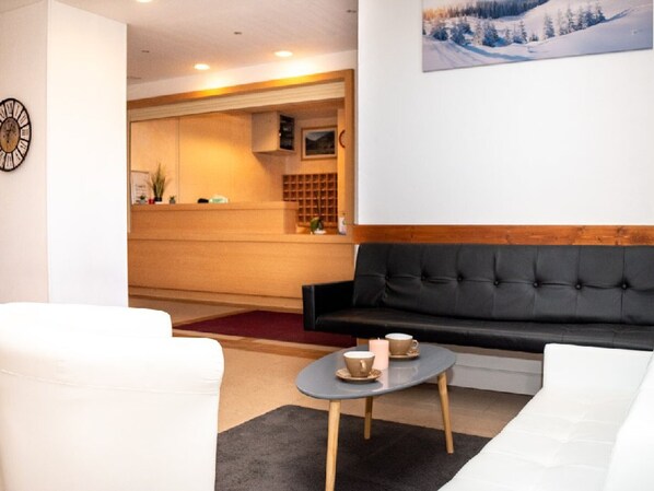 Un moderno vestíbulo de hotel con un mostrador de recepción, un sofá negro y un sillón blanco.