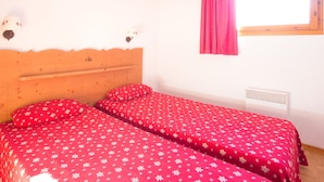 Ein Schlafzimmer mit zwei Betten, einem hölzernen Kopfteil, einem Fenster mit rosa Vorhang und einem Wandheizkörper.