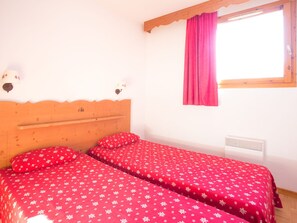 A bedroom with two beds, a wooden headboard, a window with a pink curtain, and a wall-mounted heater.