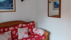 Ein Schlafzimmer mit Holz-Kopfteil, einem Bett mit roten und weißen Musterbettwäsche, einer Wandlampe und zwei gerahmten Bildern einer Berglandschaft.