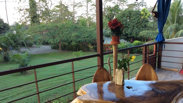 A wooden table with chairs on a balcony with a view of a garden. - Fancy holidays in paradise? Make yourself at home! (Parrita)