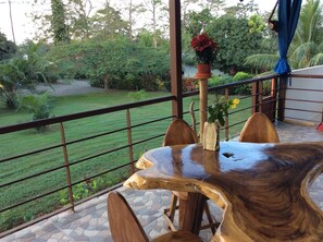 A wooden table with chairs on a balcony with a view of a garden.
