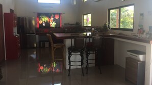 A kitchen with a refrigerator, sink, and dining area with chairs. - Fancy holidays in paradise? Make yourself at home! (Parrita)