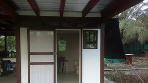 A covered outdoor area with a concrete floor, a door leading to an interior space, and a view of a palm tree and greenery outside. - Fancy holidays in paradise? Make yourself at home! (Parrita)