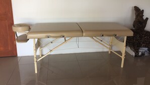 A medical examination table with a wooden frame and beige cushions, positioned in a room with a tiled floor and a wooden door. - Fancy holidays in paradise? Make yourself at home! (Parrita)