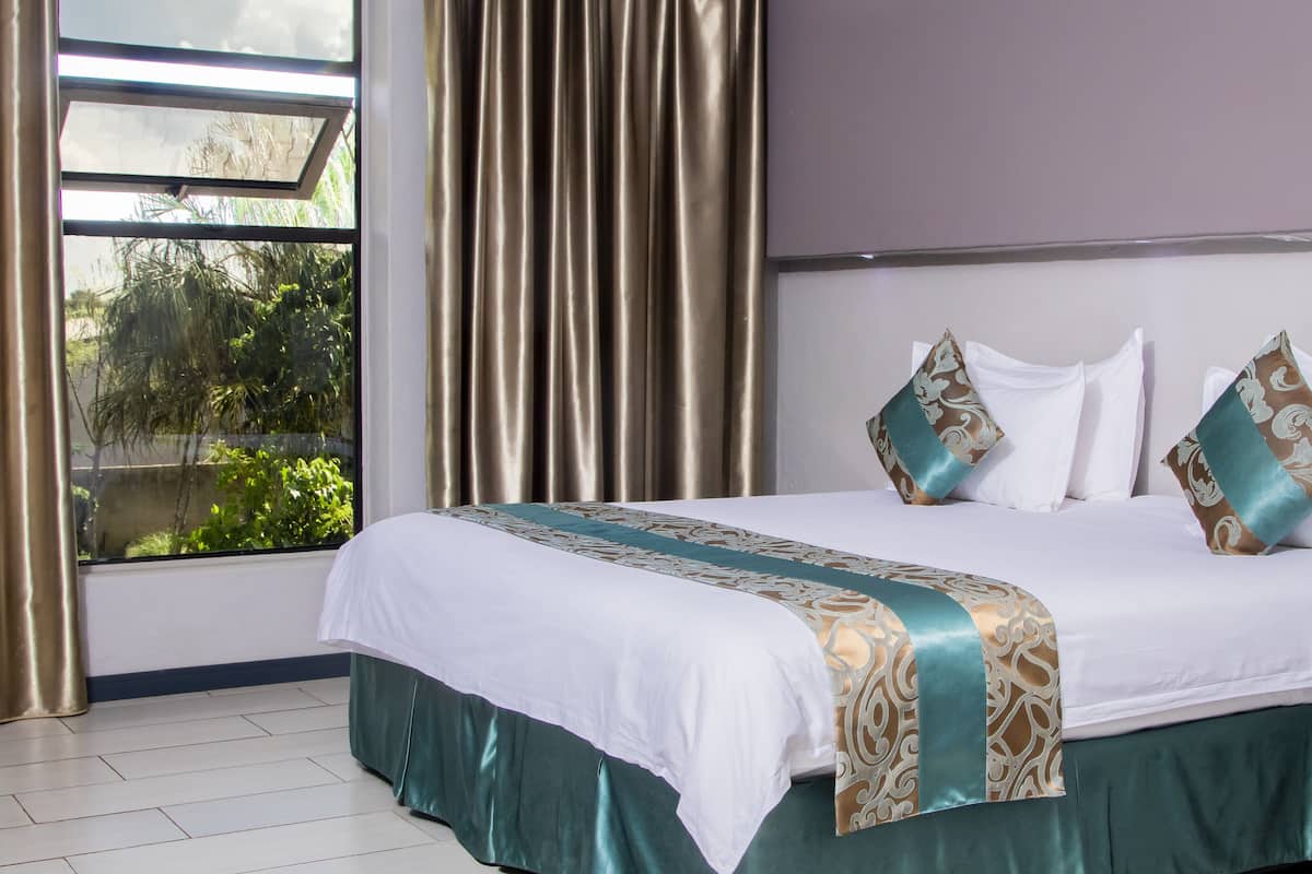 A neatly made bed with a white and green bedspread, two white pillows, and decorative pillows with a brown and green pattern.