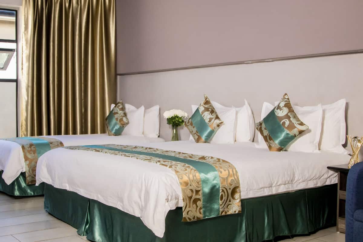 A hotel room with two beds, a large window with curtains, and a vase with flowers.