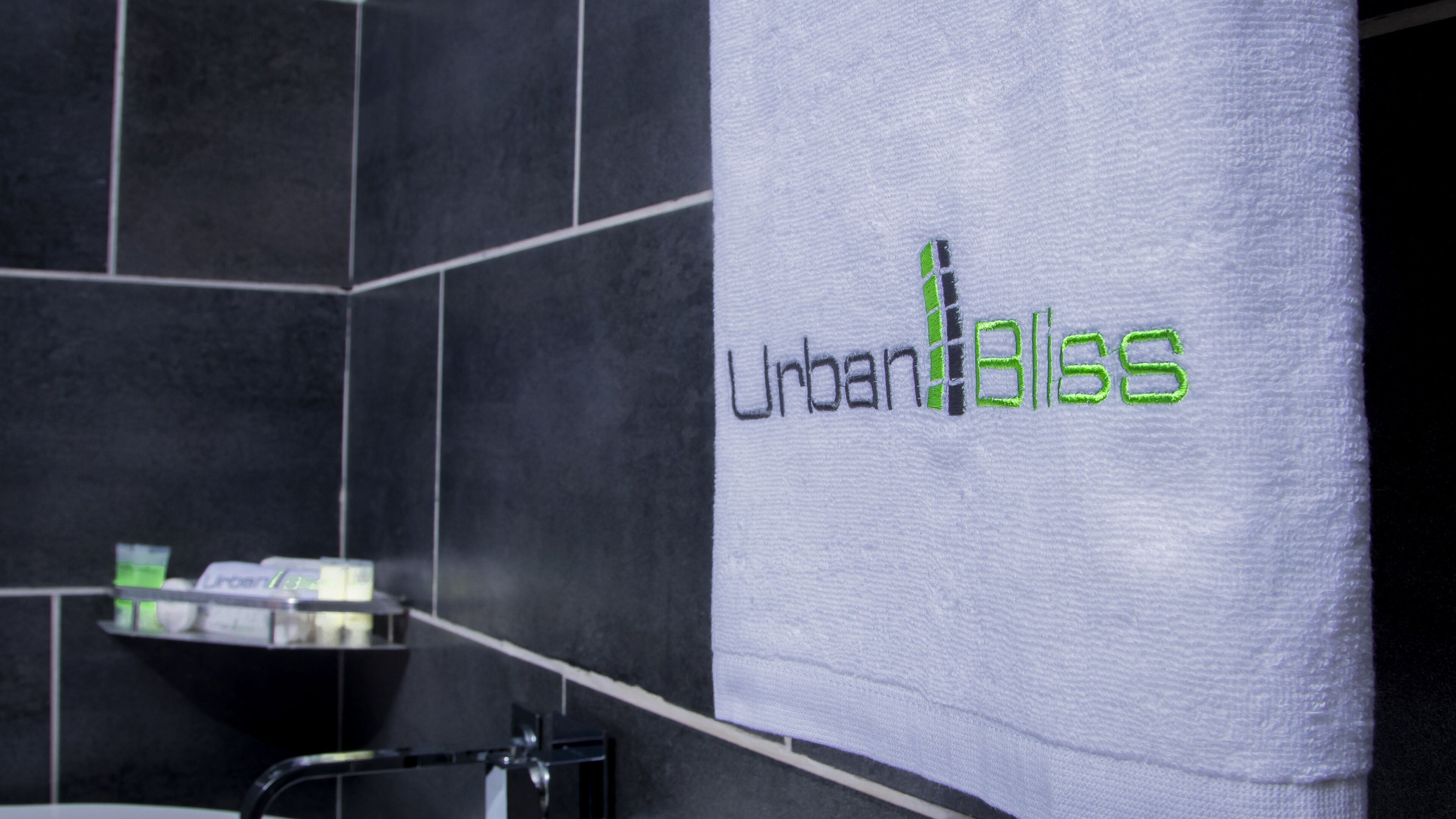 A bathroom with a towel hanging on a rack that reads "Urban Bliss" in green lettering.