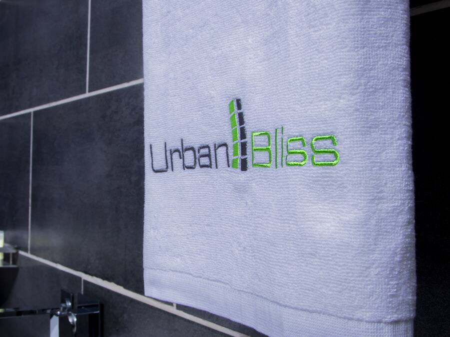 A bathroom with a towel hanging on a rack that reads "Urban Bliss" in green lettering.