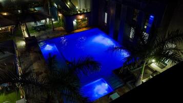 A nighttime view of a swimming pool with surrounding palm trees and a building with illuminated windows.