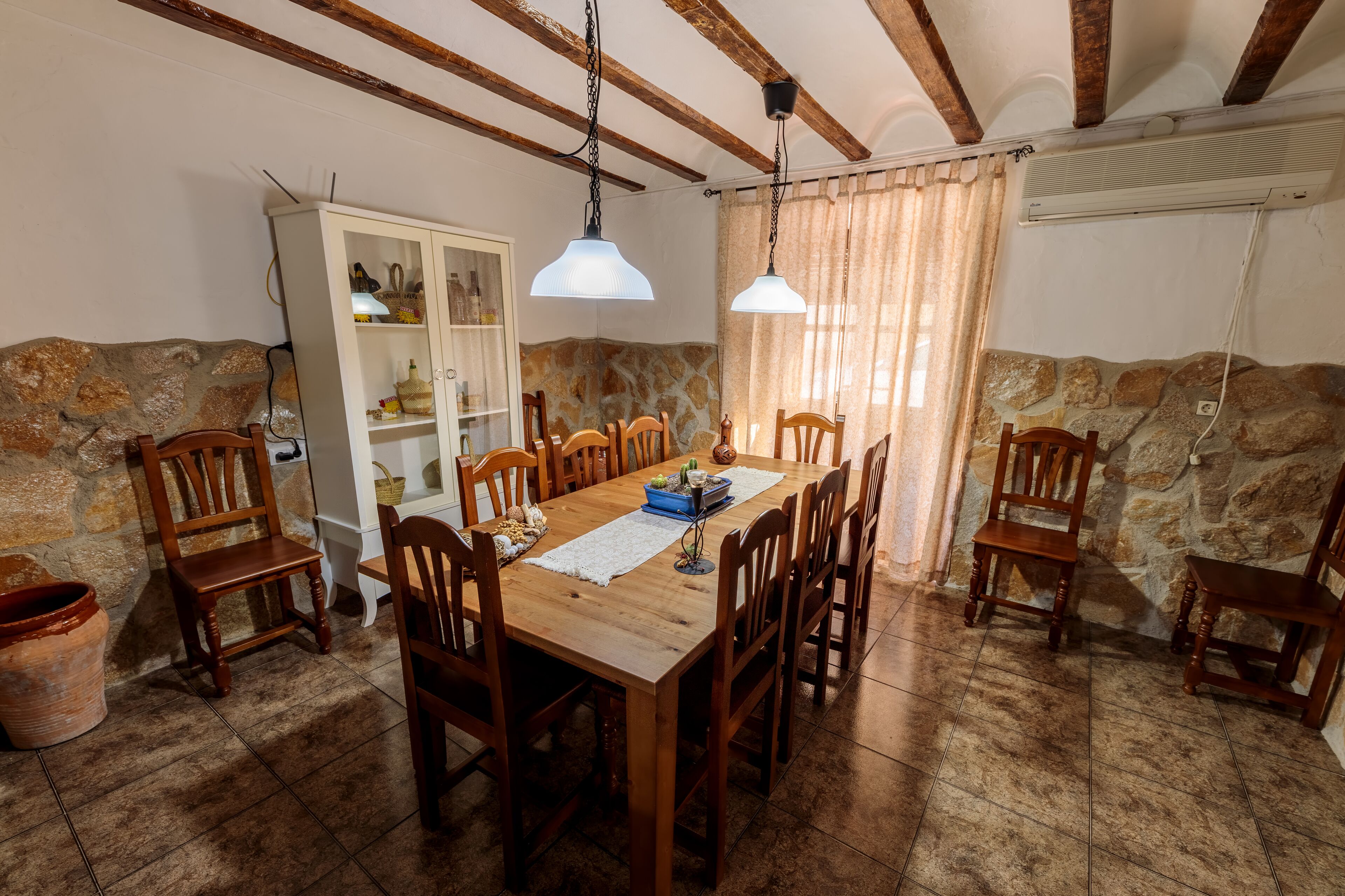 Ein Essbereich mit Holztisch und -stühlen, Steinwänden und einem weißen Schrank mit Glastüren.