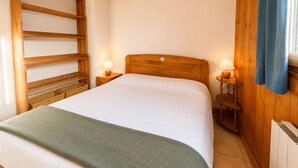 Un dormitorio con una cama, dos mesitas de noche con lámparas, cabecera de madera, escalera de madera y una ventana con cortinas.