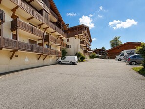 Ein mehrgeschossiges Gebäude mit Balkonen, einem Parkplatz und blauem Himmel.