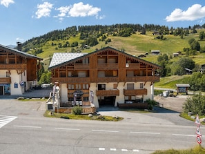 A traditional wooden chalet with a balcony, a signboard, and a paved road in front.