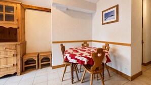 Comedor con mesa dispuesta para cuatro, sillas de madera, un pequeño aparador y un cuadro en la pared.