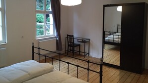 Une chambre à coucher comprenant un lit, un bureau, une chaise, un grand miroir et une fenêtre avec des rideaux.