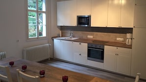 Une cuisine moderne avec des meubles blancs, un four à micro-ondes, un four et un évier. On y trouve une table à manger avec des chaises et des porte-bougies rouges.