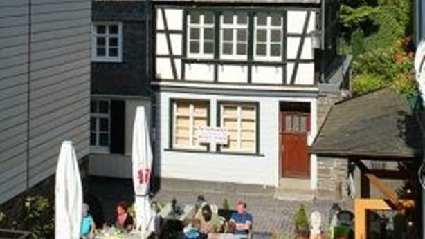 Un bâtiment traditionnel à colombages, doté d’une tour centrale, de nombreuses fenêtres et d’un espace extérieur aménagé avec des tables et des parasols.