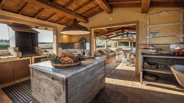 Une cuisine rustique dotée d’un grand îlot central, de poutres en bois et offrant une vue sur l’extérieur.