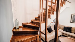 En trætrappe fører op til en anden etage, en beige sofa med sorte puder, og et indrammet kunstværk på væggen.