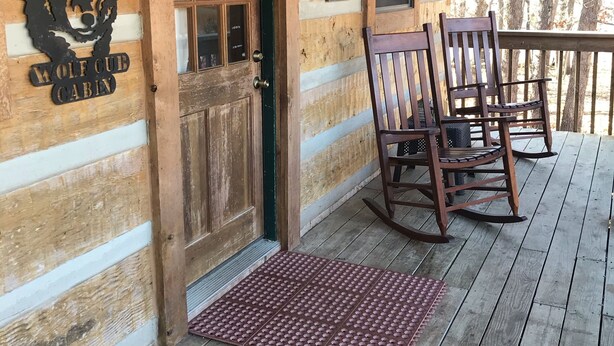 A cabin entrance with a wooden door, a wolf head cutout, and a sign listing rules.