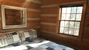 A log cabin room with a bed, a window, and a mirror.