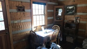 A cabin interior with a dining table, chairs, a sofa, a window, and a wooden wall with a welcome sign.