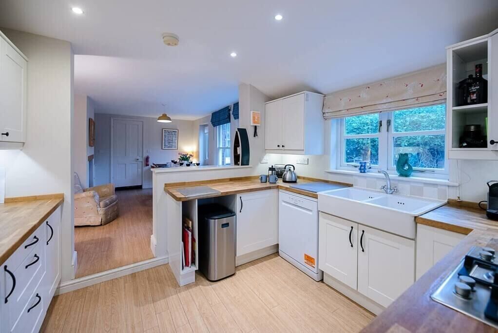 A modern kitchen with white cabinetry, a built-in dishwasher, and a window providing natural light.