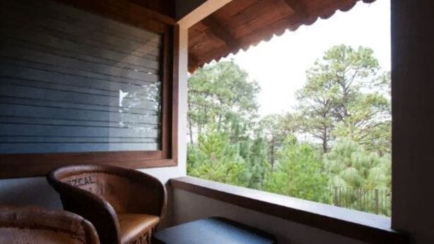 A room with a wooden ceiling, a window with a view of trees, two wooden chairs, and a small table. - Perfect for honeymoon C10 (Lázaro Cárdenas)