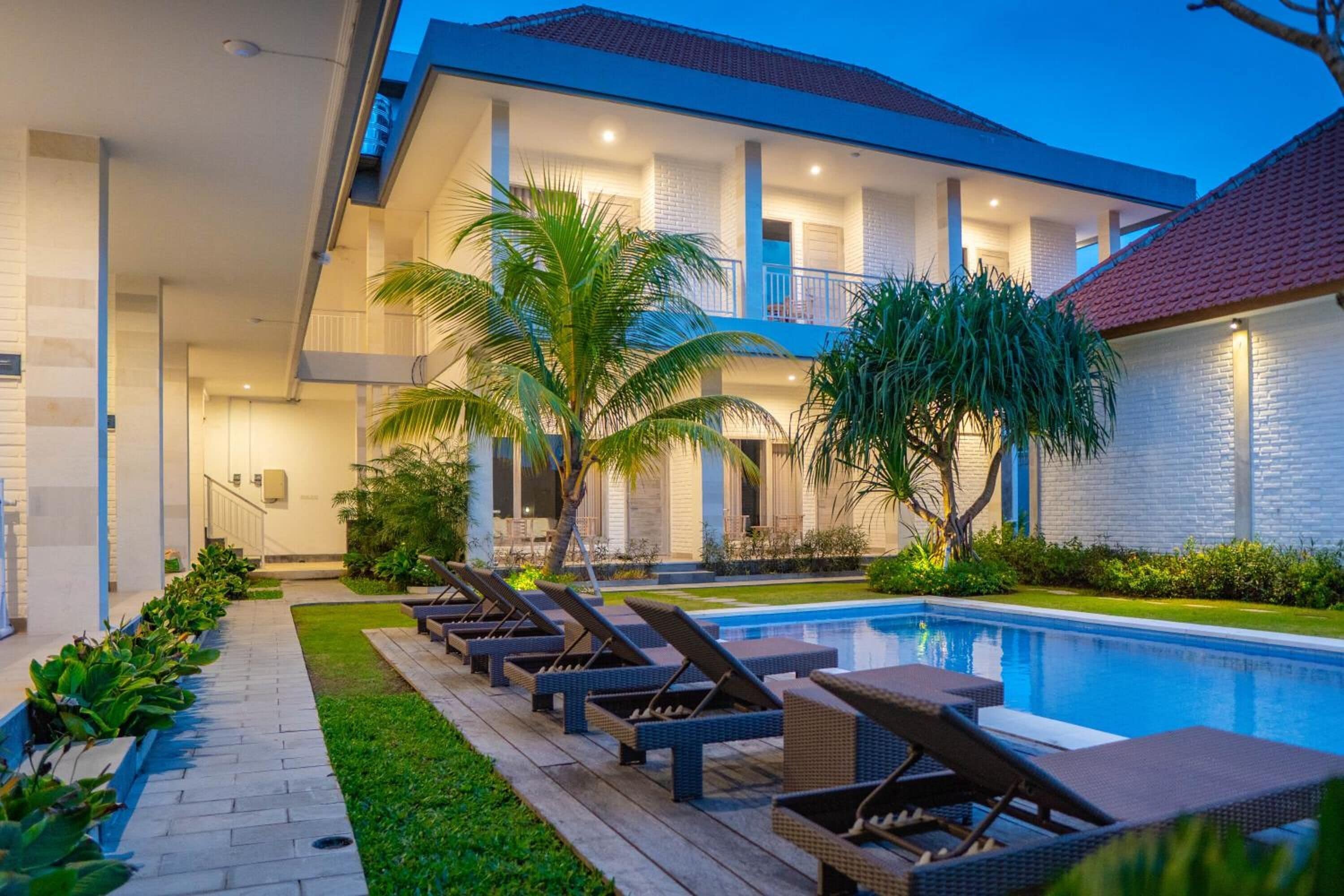 A modern hotel with a swimming pool, lounge chairs, and a well-maintained garden.