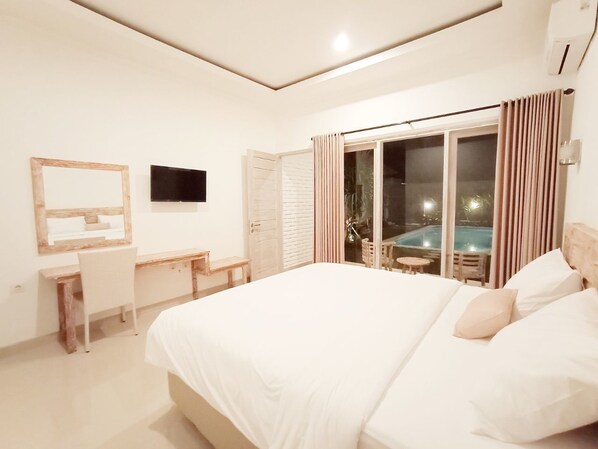 A bedroom with a large bed, a desk, a chair, a TV, and a sliding glass door leading to a pool area.