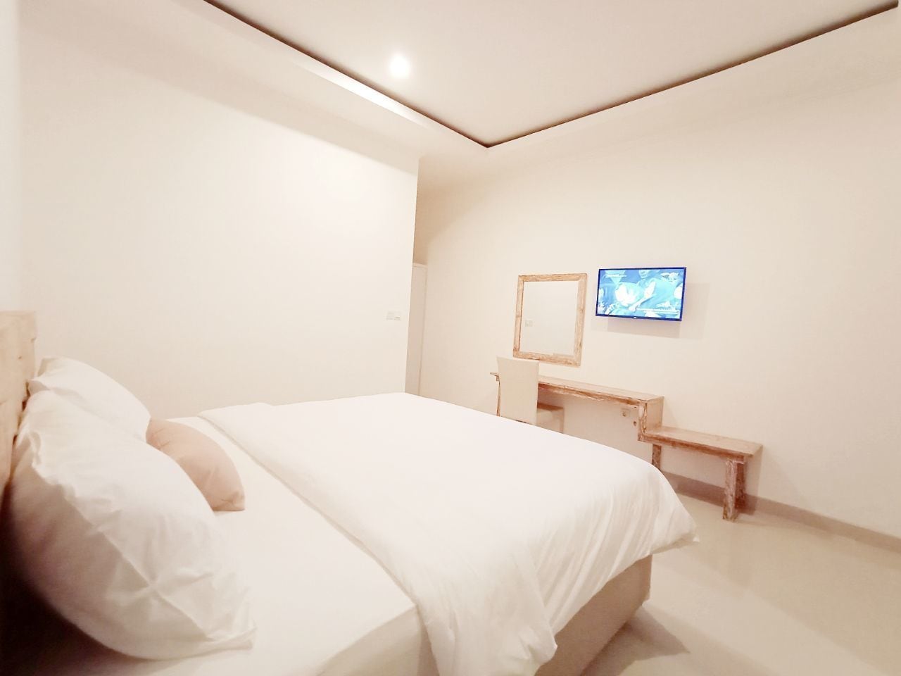A minimalist bedroom with a bed, a desk, and a television on the wall.