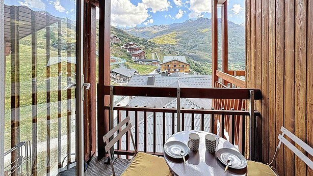 En balkon med et bord dækket til to, med udsigt over et bjerglandskab med bygninger.