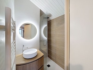 A modern bathroom with a round mirror, a white sink, and a glass-enclosed shower.