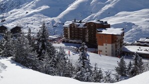 Et snedækket feriested med flere bygninger, heriblandt en markant lodge med stolelift i baggrunden.