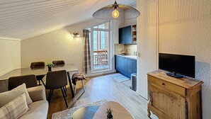 En moderne stue med spiseplads, et køkken og et fjernsyn på et træskab.
