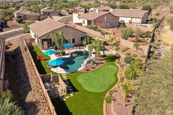 A residential area with a large house featuring a swimming pool, a golf course, and a well-maintained lawn.