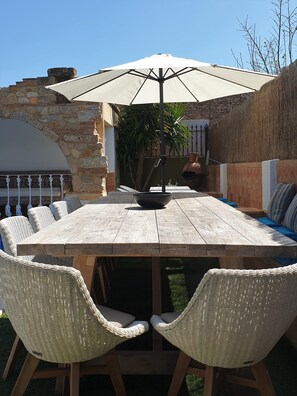 A wooden outdoor dining table with a large umbrella, surrounded by wicker chairs.