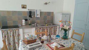 A small kitchen with a dining area. The kitchen has a sink, a stove, and a refrigerator. The dining area has a table with chairs and a vase with flowers. - Chez Bonjour: holiday home with large terrace overlooking the mountains (Villar Pellice (TO))