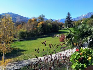 Un exuberante jardín con un camino de piedra, rodeado de árboles con follaje otoñal y un telón de fondo montañoso.
