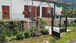 A white building with brown shutters, a gated entrance, and a garden with various plants and flowers. - Chez Bonjour: holiday home with large terrace overlooking the mountains (Villar Pellice (TO))