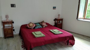 A neatly made bed with a red bedspread, two pillows, and two folded towels. There are two bedside tables with lamps and a small picture on the wall. - Chez Bonjour: holiday home with large terrace overlooking the mountains (Villar Pellice (TO))