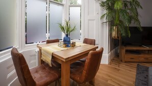 A dining area with a wooden table, brown leather chairs, a blue vase with green plants, and a window with frosted glass. - Bootham Luxury Apartments Flat 2 (York)