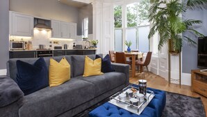 A modern living room with a grey sofa, blue ottoman, and a coffee table with a tray of mugs and pastries. - Bootham Luxury Apartments Flat 2 (York)