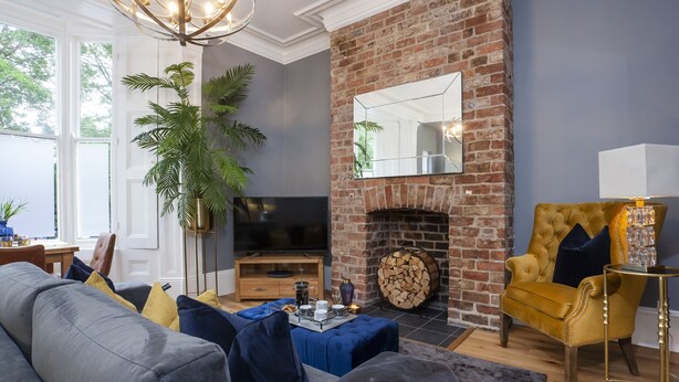 A living room with a brick fireplace, a large mirror, a television, and a comfortable seating area. - Bootham Luxury Apartments Flat 2 (York)