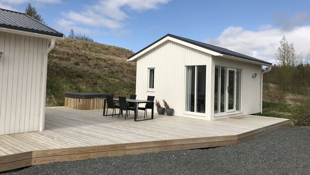 A modern cabin with a wooden deck, a hot tub, and a dining area.