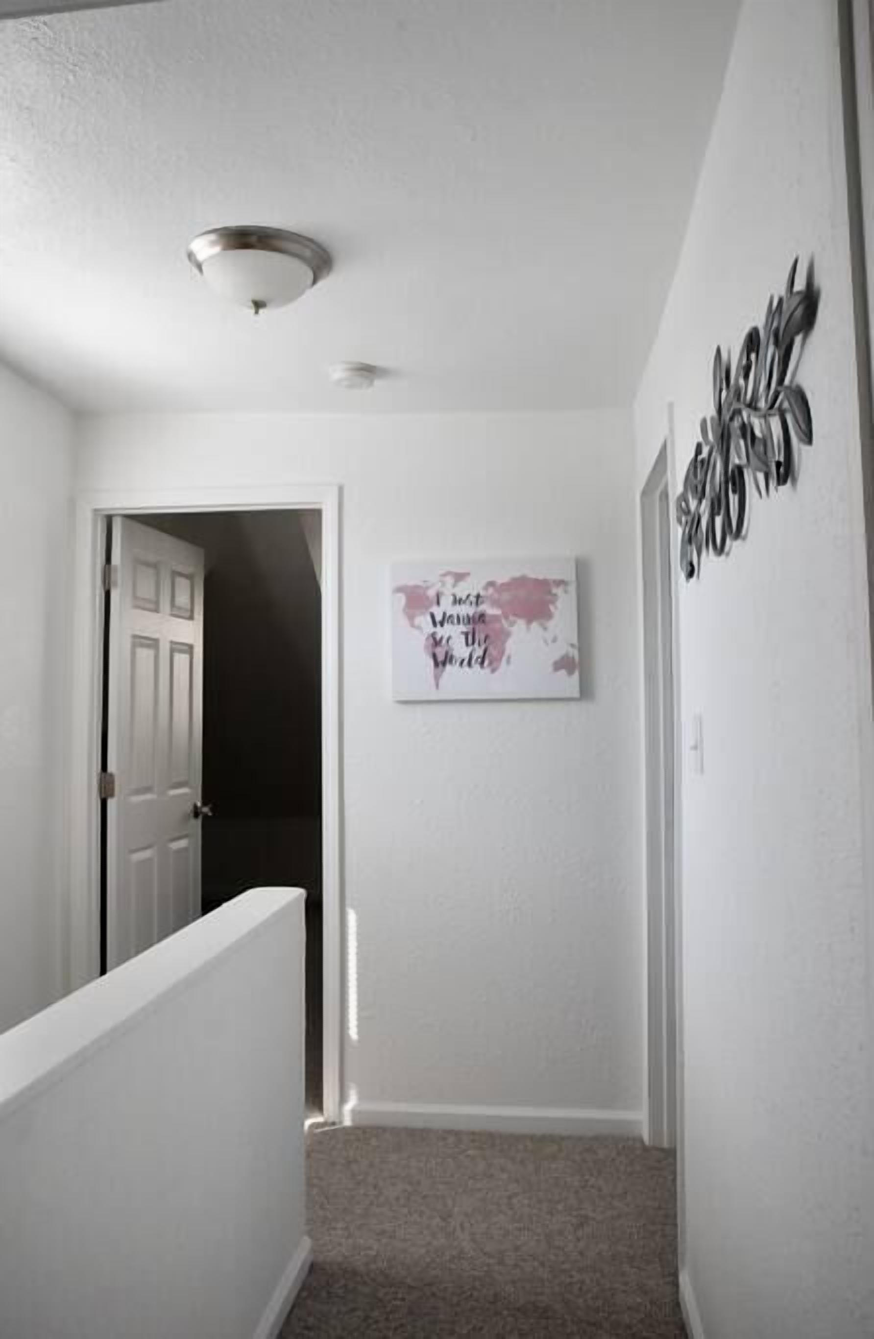 A narrow hallway with a white door at the end, a ceiling light, and a world map poster on the wall.