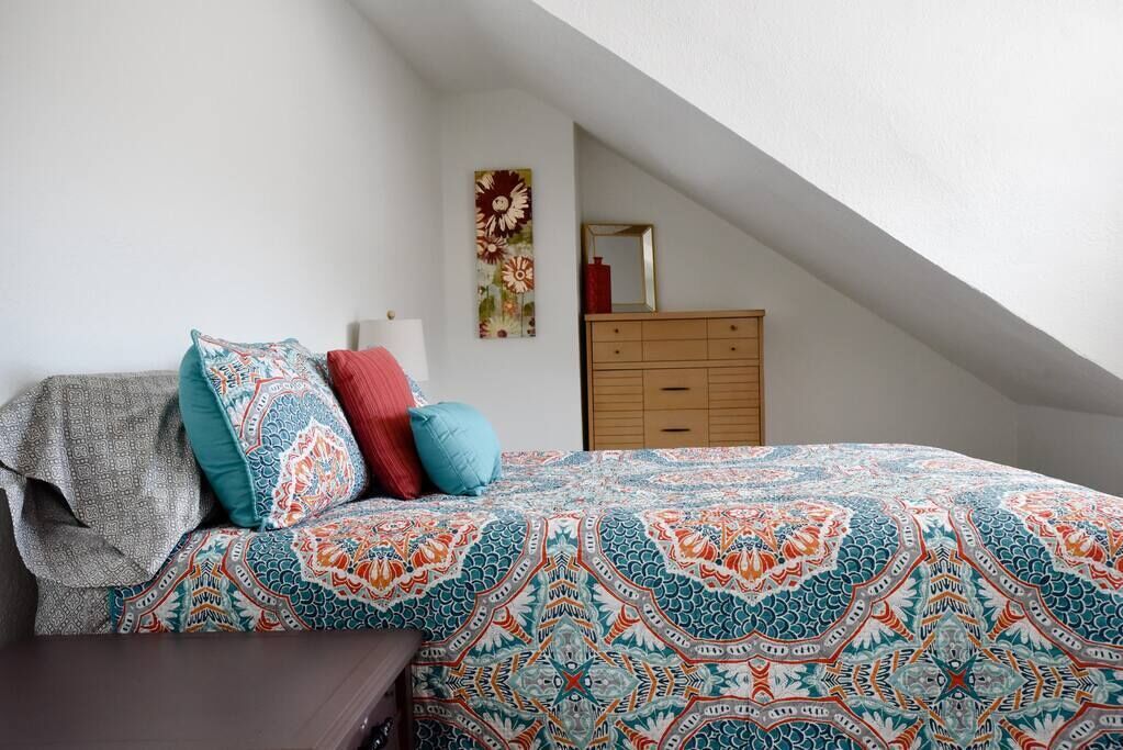 A bedroom with a patterned bedspread, a wooden dresser, and a mirror.